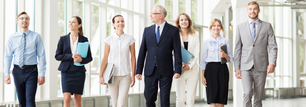 Eine Gruppe von Geschäftsleuten, angeführt von einem älteren Mann im Anzug, geht gemeinsam nach draußen.