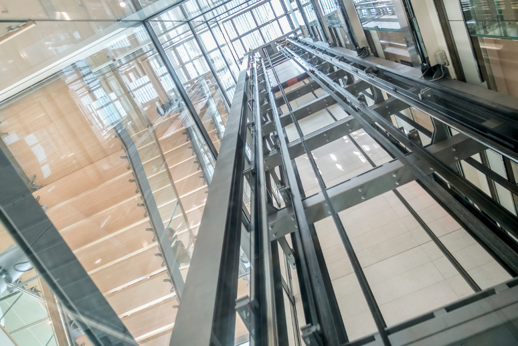 Ein Blick in ein modernes Treppenhaus mit Glasgeländern und Aufzugsschacht.